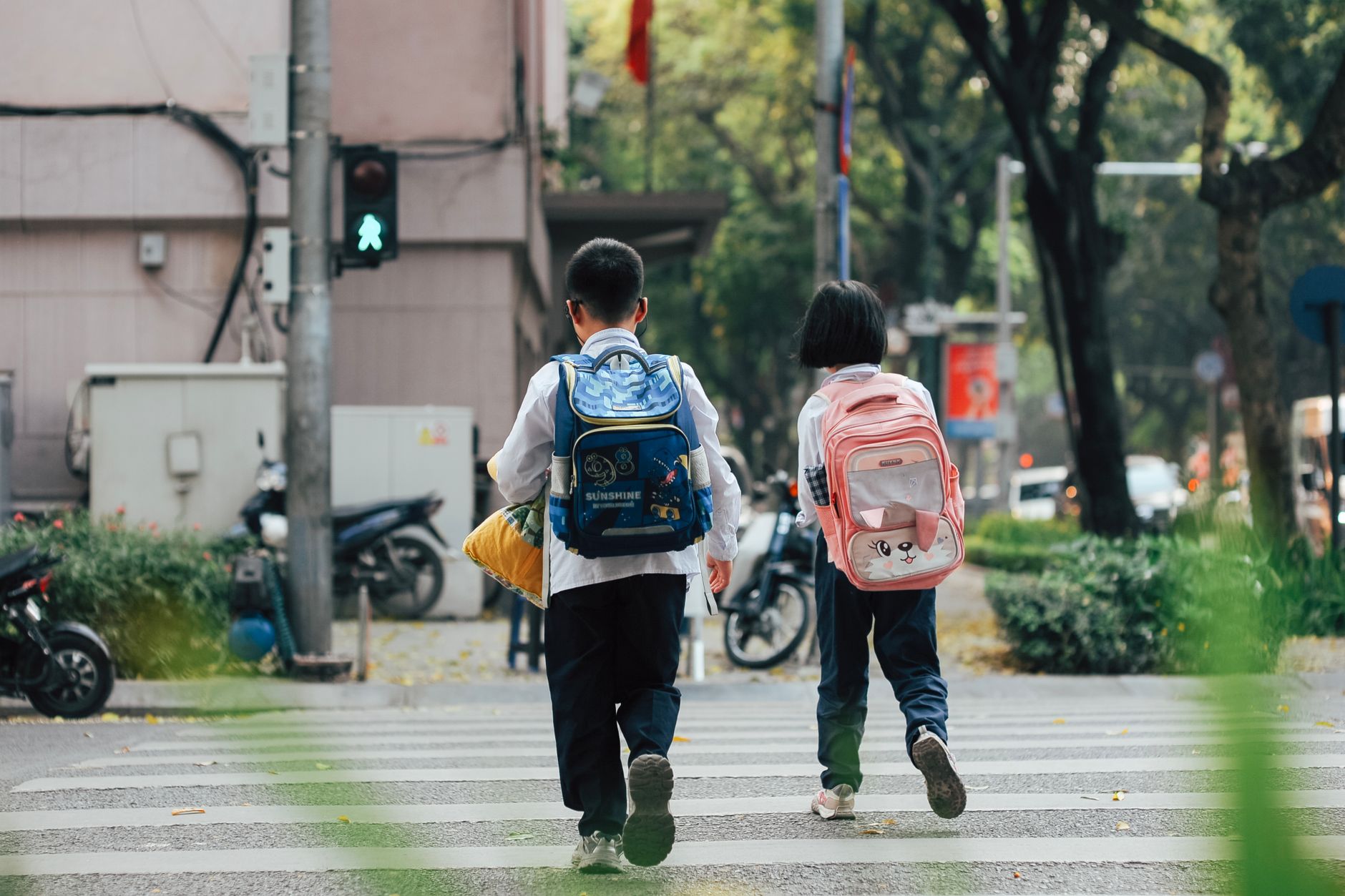 Two children with backpacks crossing a street at a pedestrian crosswalk.