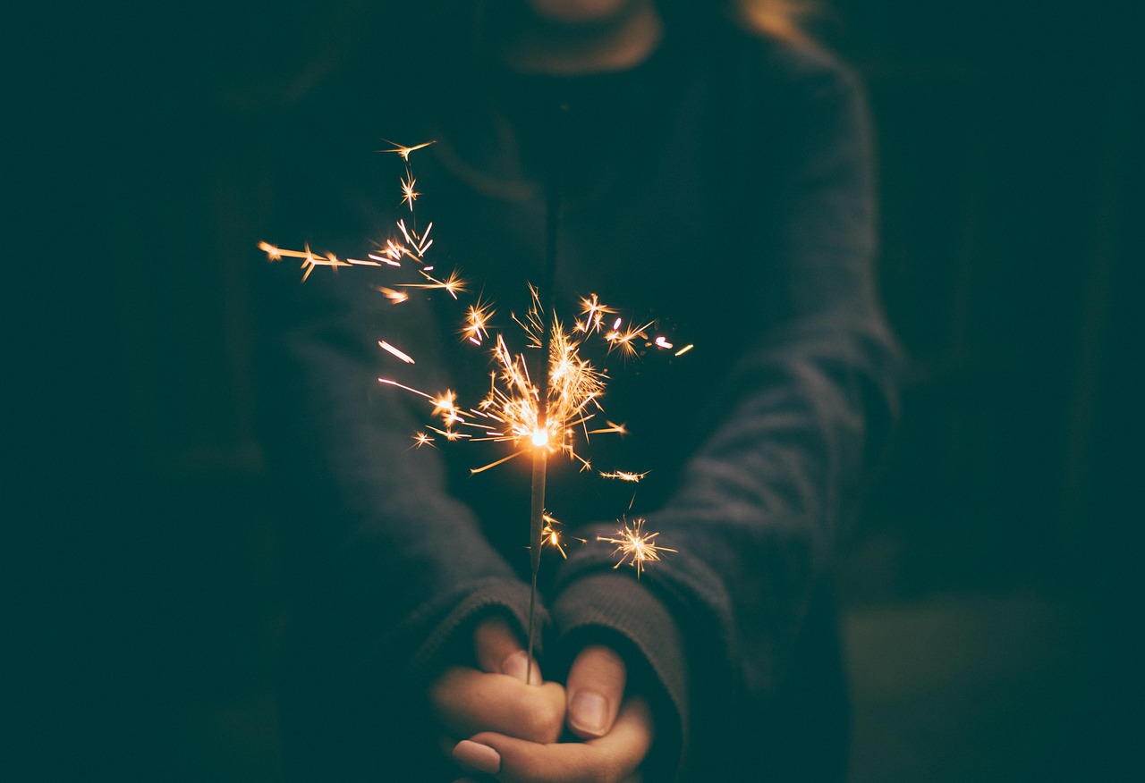 A hand holding a sparkler at night.