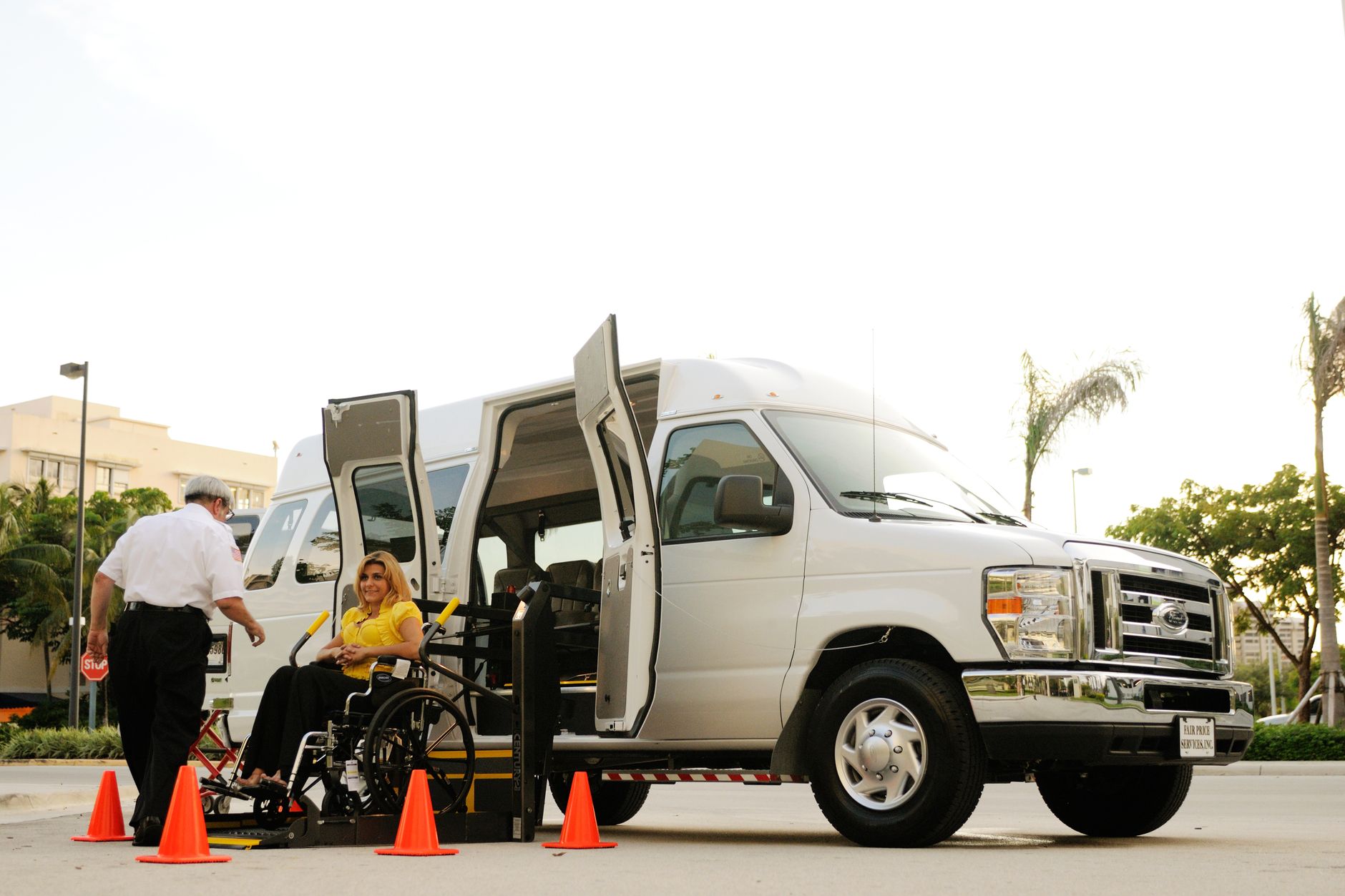 A person in a wheelchair boards a van using a lift, assisted by a driver.