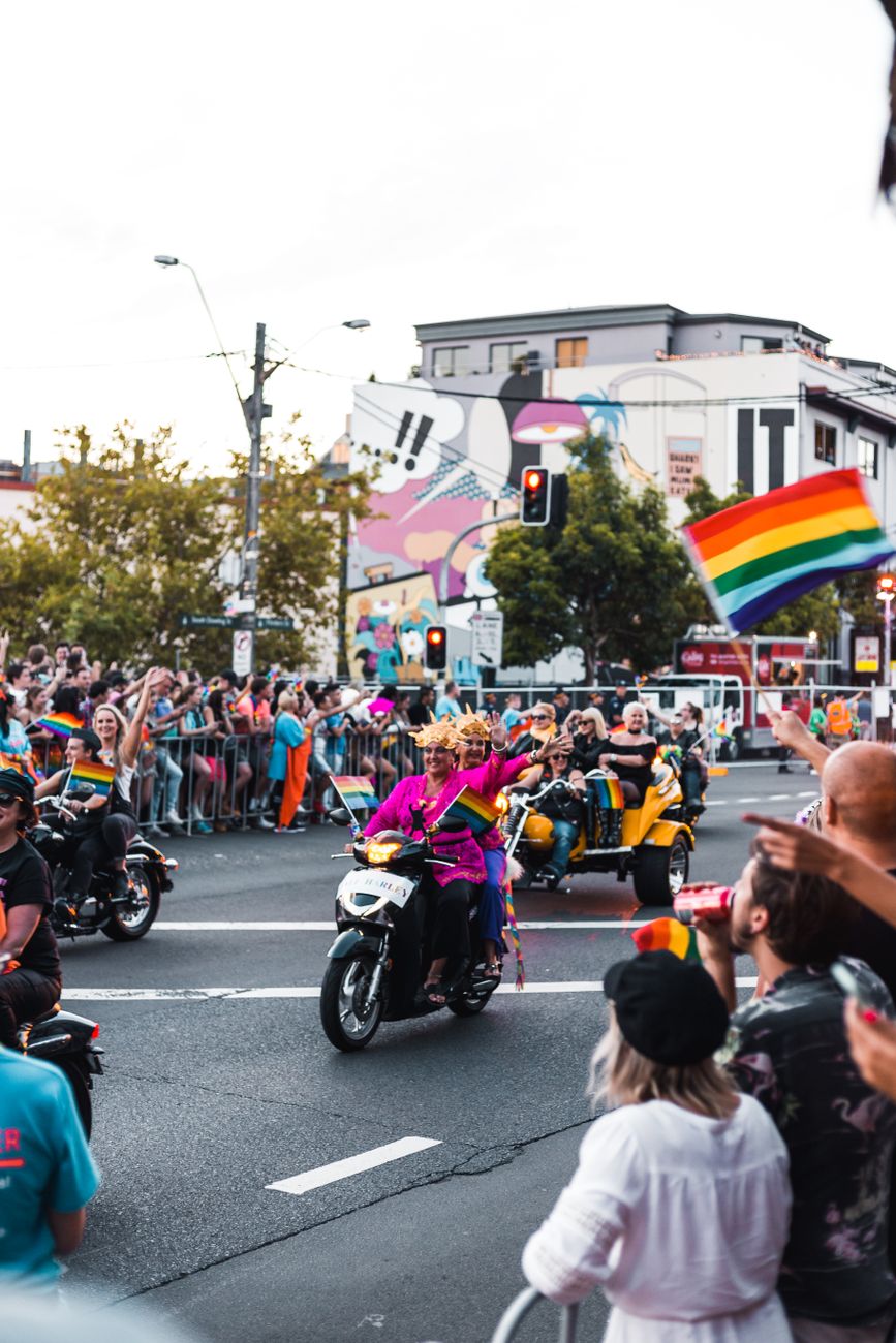 People on motorcycles and pedestrians in a pride parade on a city street.