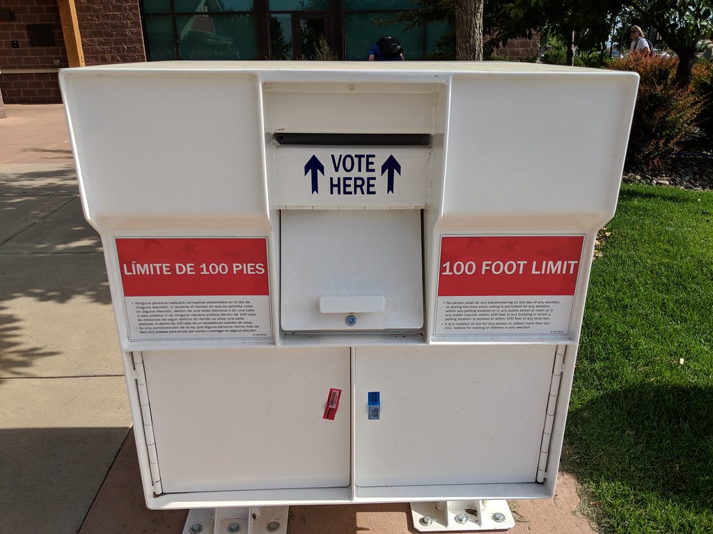 A ballot box beside a “VOTE HERE” sign at a Colorado polling location.