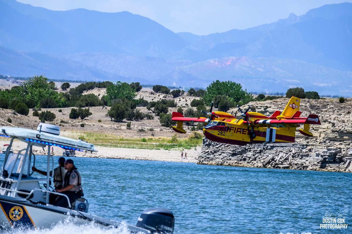 A firefighting aircraft approaches the surface of Lake Pueblo as officers in a boat help maintain a safe operating area.