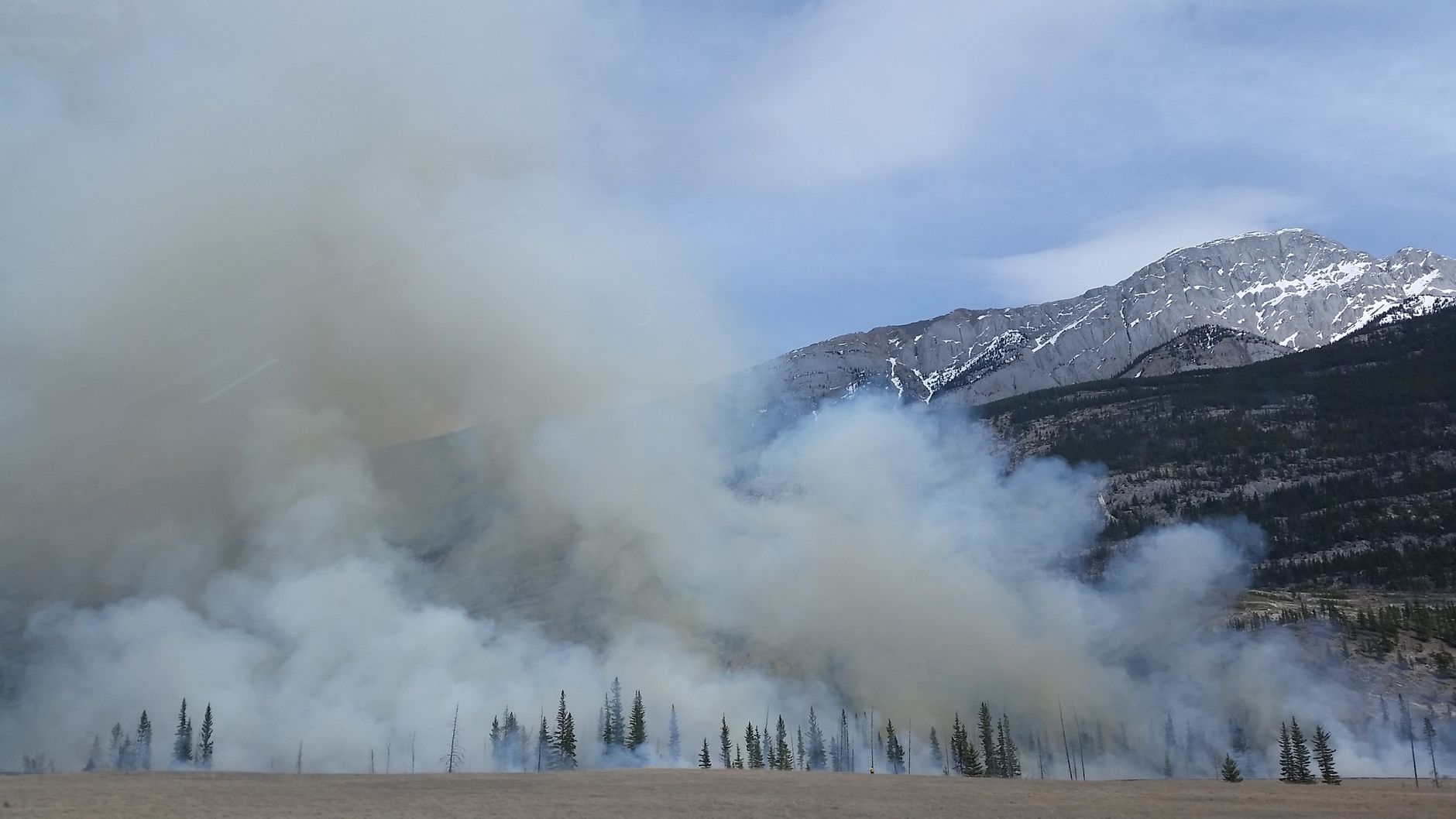 Smoke rises from a forested mountain landscape.