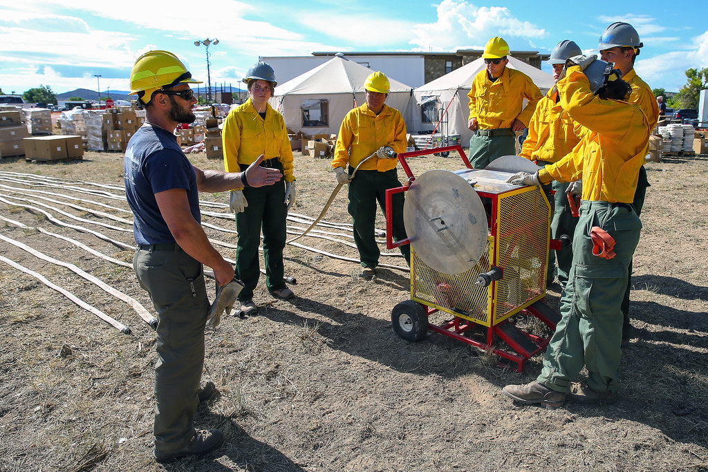Firefighters work with hose equipment during wildfire suppression in a dry, wooded landscape.