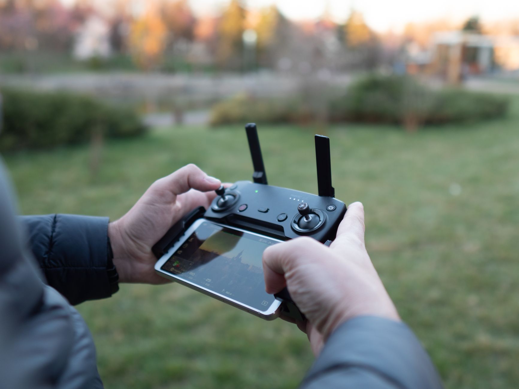 Hands operate a drone controller with a smartphone attached outdoors.