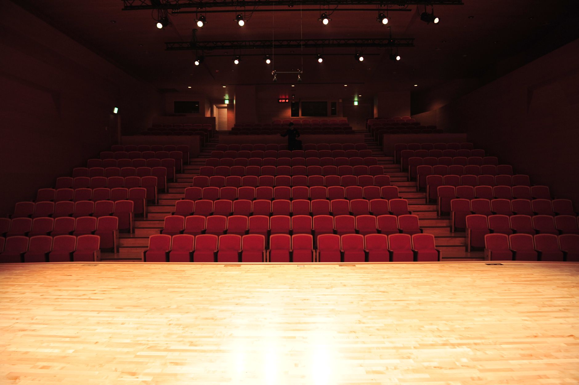 Empty theater auditorium with rows of red seats facing an illuminated stage.