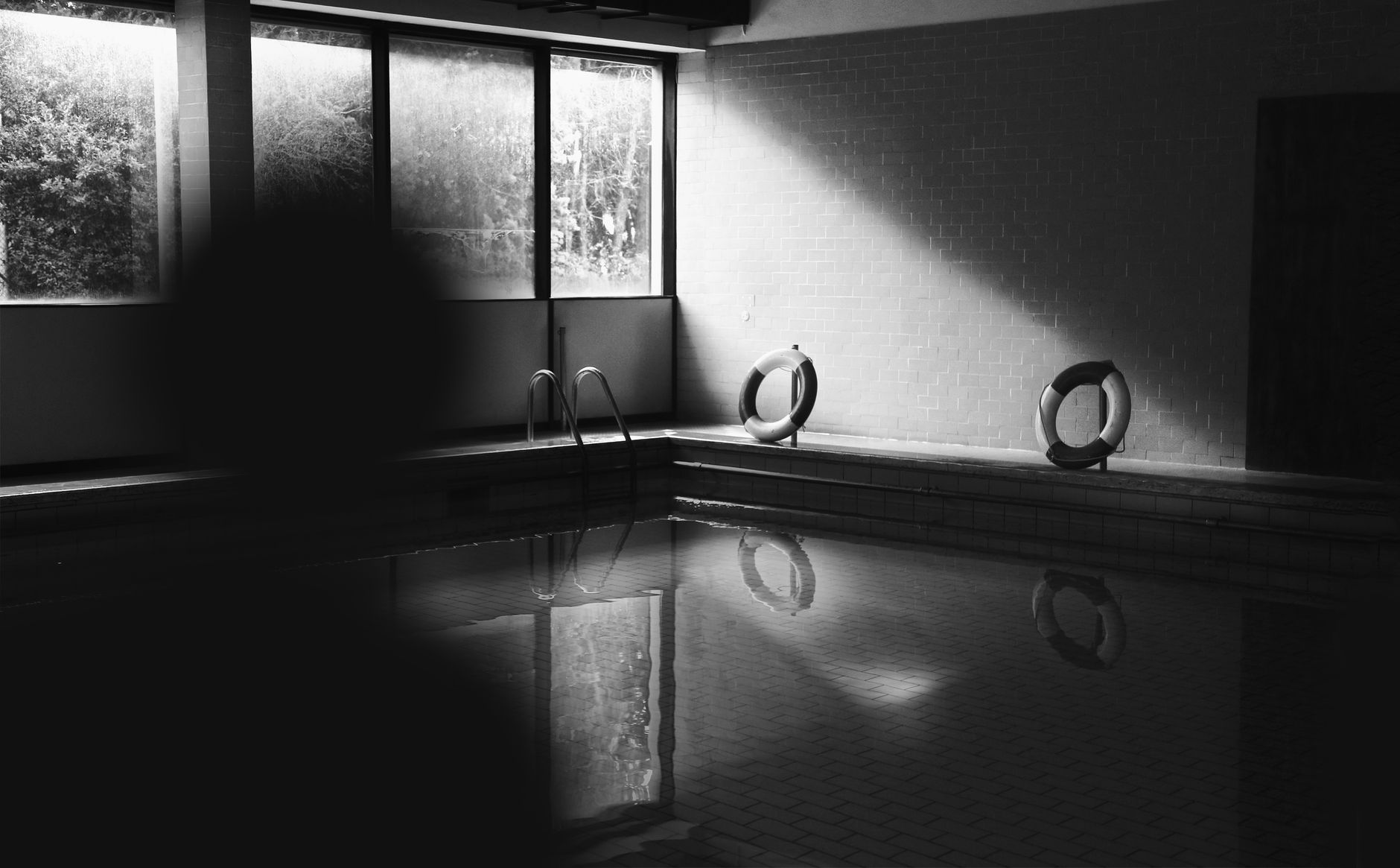 An empty indoor pool area with lifebuoys and reflections on the water.